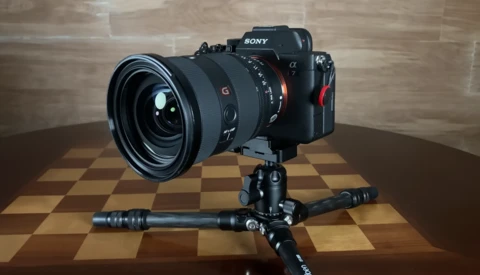 Sony mirrorless camera with wide-angle lens mounted on tripod with ball head against checkered backdrop.
