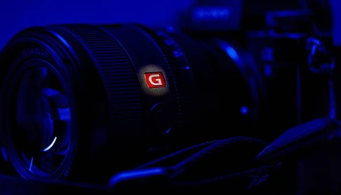Sony G-series camera lens illuminated by blue ambient light against dark background.