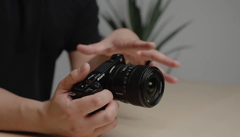 Hands holding a black mirrorless camera with a wide-angle lens attached.