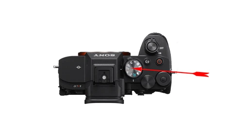 Top-down view of a Sony mirrorless camera with mode dial and control buttons highlighted.