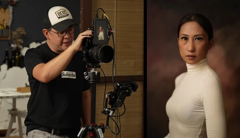 Photographer adjusting a studio light setup while shooting a portrait of a woman in a white turtleneck.
