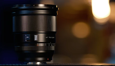 Black telephoto lens with autofocus markings, shot against warm bokeh background lighting.