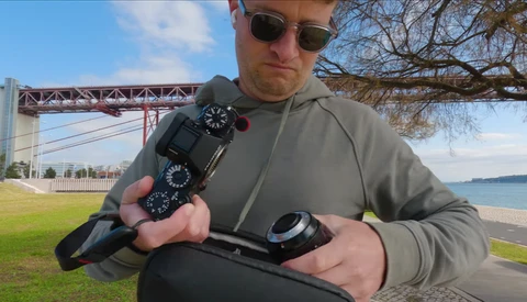 Photographer holding camera gear and wireless transmitter outdoors near a bridge and waterfront.