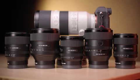 Collection of five prime lenses arranged in front of a telephoto zoom lens and camera body against warm studio lighting.