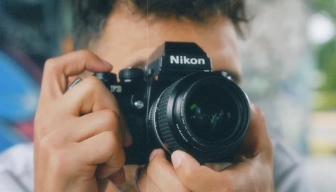 Photographer holding a Nikon DSLR camera up to their face to compose a shot.