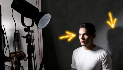Man in white t-shirt positioned in front of professional studio lighting setup with yellow neon arrows.
