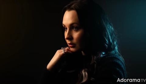 Woman with long dark hair in dramatic low-key studio lighting, gazing downward with contemplative expression.