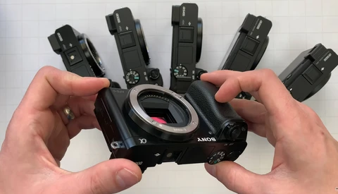 Sony mirrorless camera body held in hands with five wireless flash units displayed above it.