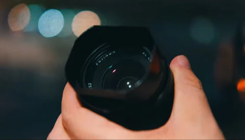 Hand holding a wide-angle camera lens with bokeh lights blurred in the background.