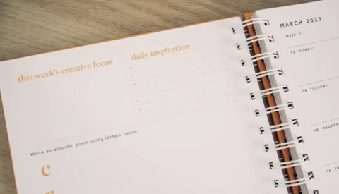 Open spiral-bound planner showing March 2023 week layout with creative writing prompts and daily inspiration sections.