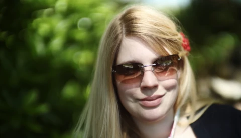 Young woman wearing oversized sunglasses and dark clothing outdoors in natural daylight.