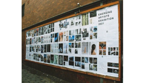 Large outdoor gallery wall displaying numerous photographs and artworks arranged in a grid layout with an orange frame border.
