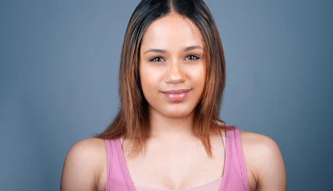 Woman with long dark hair wearing a pink tank top against a blue-gray backdrop.