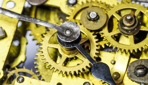 Close-up of brass watch movement gears and escape wheel lever against yellow metal plates.