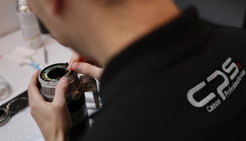 Photographer in black shirt examining a camera lens up close.