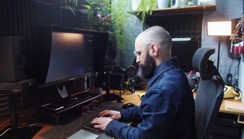 Bearded man working at a computer setup in a creative studio workspace.