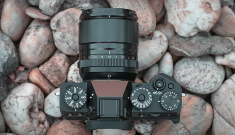 Camera with attached lens mounted on rocky surface, viewed from above.