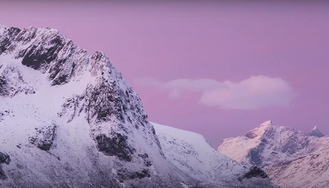 Snow-covered mountain peaks under a dramatic purple and pink sky at dusk or dawn.