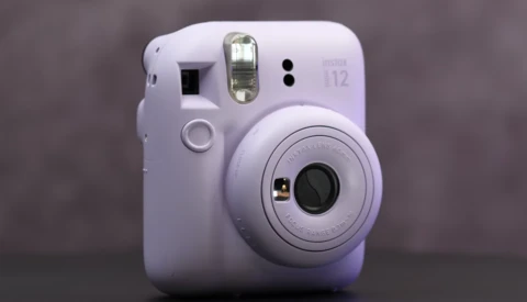 White Fujifilm Instax Mini 12 instant camera with flash and lens visible against neutral background.