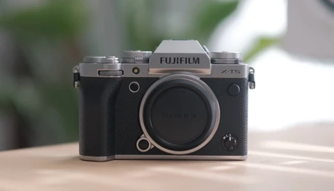 Fujifilm X-T5 mirrorless camera body displayed front-on against a blurred outdoor background.