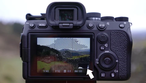 Mirrorless camera displaying live view of a rural building with metal roof and surrounding landscape on its rear LCD screen.