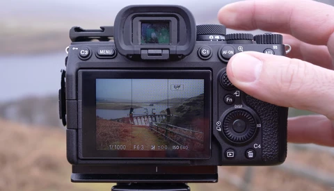 Sony mirrorless camera held in hand showing coastal landscape in LCD screen and electronic viewfinder.