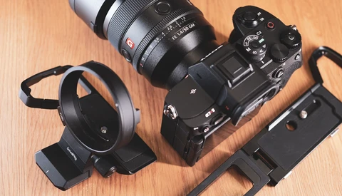 Sony mirrorless camera with attached lens, lens hood, and mounting bracket on wooden surface.