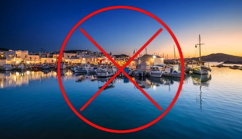 Red prohibition symbol overlaid on a Mediterranean harbor at twilight with boats and illuminated waterfront buildings.