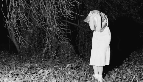 Woman in white dress standing beneath hanging willow branches in dark nighttime setting.