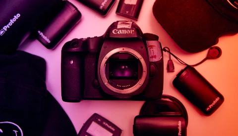 Canon DSLR camera body with batteries and accessories arranged on a pink and orange gradient background.