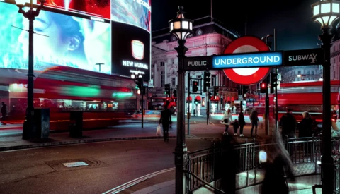 London Underground station entrance at night with neon signage and red double-decker bus in motion blur.