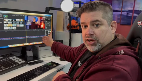 Video editor gesturing at color-graded footage on dual monitors in a studio workspace.