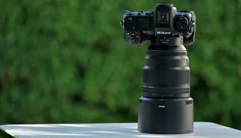 Nikon camera with telephoto lens mounted on white surface against blurred green background.