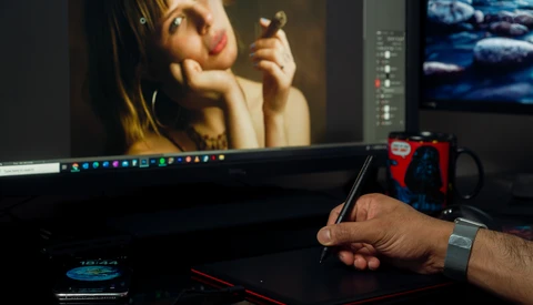 Photo editor's hand holding a stylus while working on a portrait image displayed on a monitor.