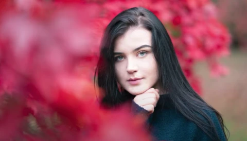 Young woman with long dark hair posing among vibrant pink flowering bushes.