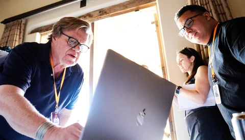 Three people gathered around a laptop computer indoors, examining the screen together.