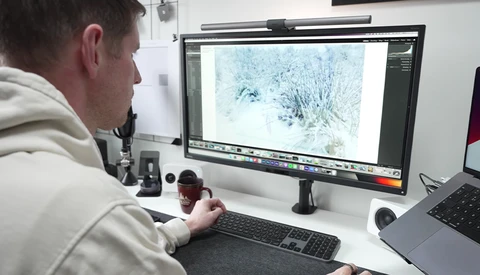 Photographer reviewing snowy landscape image on desktop monitor using image editing software.