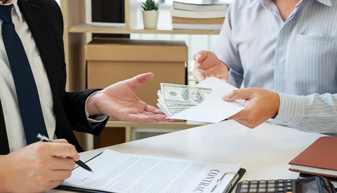 Two businesspeople exchanging cash and documents at a desk during a transaction.