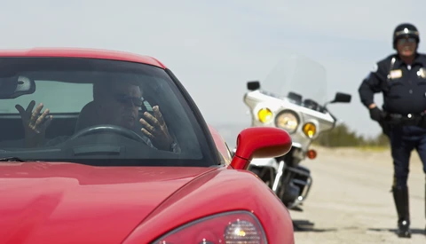 Traffic stop scene with red car in foreground and motorcycle officer in background on open road.