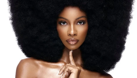 Woman with voluminous black afro hair looking directly at camera with neutral expression.