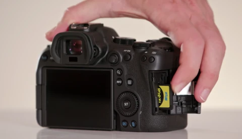 Hand inserting a yellow XQD memory card into the card slot of a professional mirrorless camera.