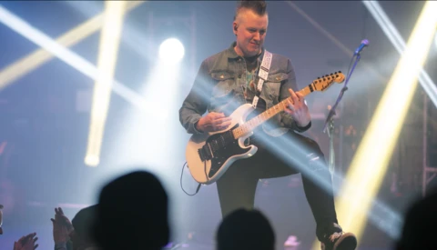 Guitarist performing on stage with electric guitar under dramatic blue and white stage lighting.