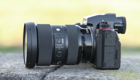 Mirrorless camera with wide-angle zoom lens mounted, positioned on a concrete surface against a blurred yellow-green background.