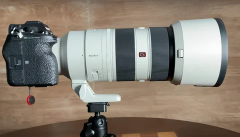 Sony telephoto lens mounted on camera body positioned on tripod against wooden surface.