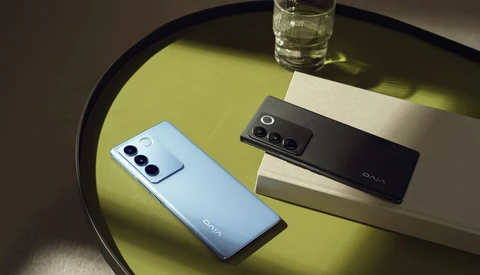 Two smartphones with triple rear camera setups displayed on a yellow-green surface next to a glass of water.
