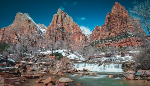 Turquoise river with small waterfall flowing through red rock canyon formations under clear blue sky.