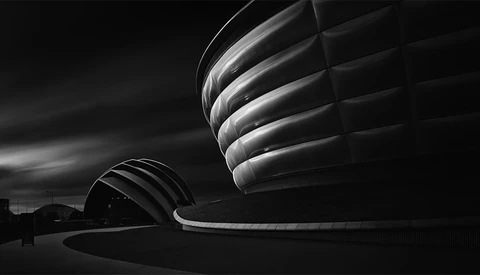 Spiral architectural forms lit dramatically against a dark sky in high-contrast black and white.