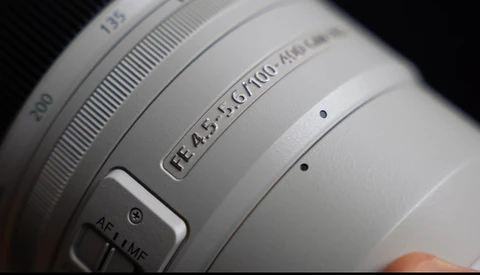 Close-up of a white camera lens showing aperture range f/4.5-5.6, focal length 67-100mm, and AF/MF focus mode switch.