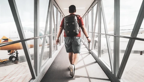 Runner jogging through a glass-walled airport jet bridge toward an airplane.