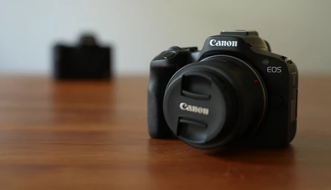 Canon EOS mirrorless camera body without lens on wooden surface, with blurred camera in background.